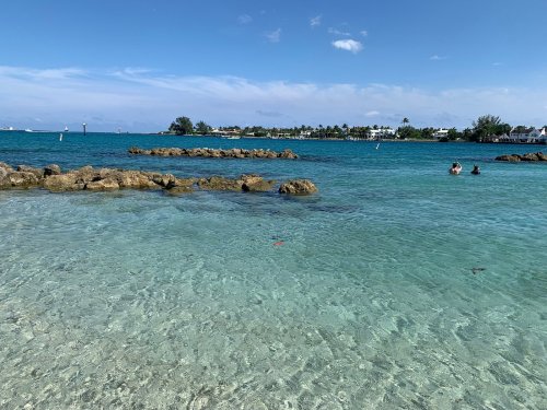 A clear blue ocean with rocky formations and two people swimming in the distance under a sunny sky.