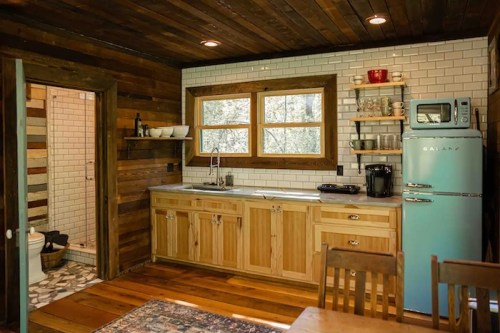 Cozy kitchen with wooden cabinets, a retro blue fridge, and a dining area, featuring natural light from windows.