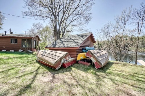 A cabin by a river with stacked boats in the foreground and trees in the background on a sunny day.