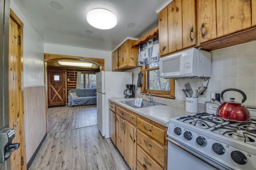 Cozy kitchen with wooden cabinets, a gas stove, and a view into a living area with a sofa and rustic decor.