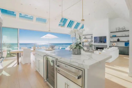 Bright, modern kitchen with a marble island, ocean view, and large windows letting in natural light.