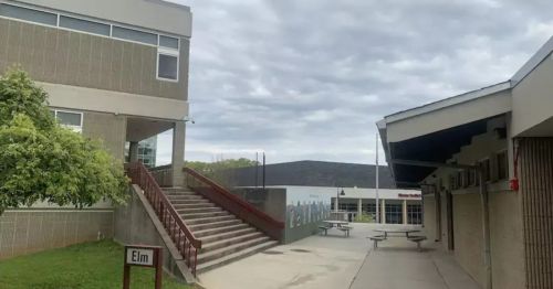 A school courtyard featuring stairs, picnic tables, and a cloudy sky. The building has a sign labeled "Elm."