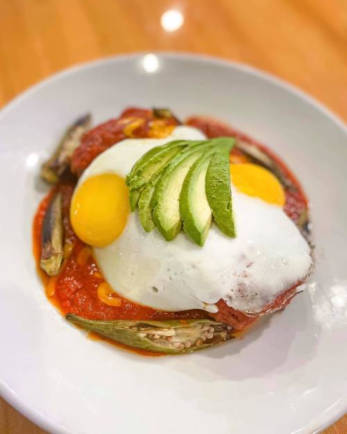 A plate of eggs topped with avocado slices, served on a bed of tomato sauce and vegetables.