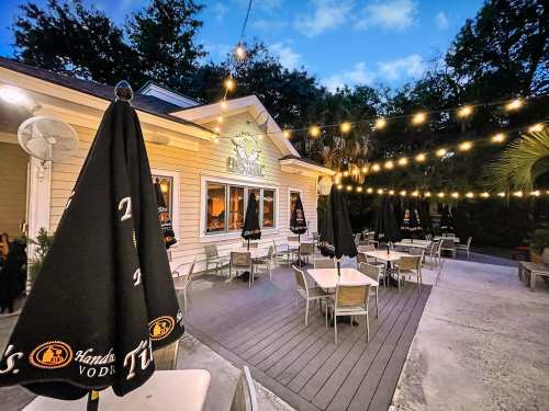 Outdoor dining area with tables, umbrellas, and string lights, set against a charming building and evening sky.