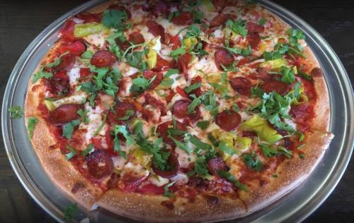 A freshly baked pizza topped with pepperoni, green peppers, and fresh cilantro on a golden crust.