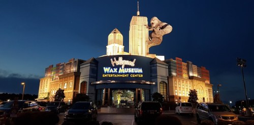 A brightly lit wax museum with a giant gorilla statue on top, set against a twilight sky.