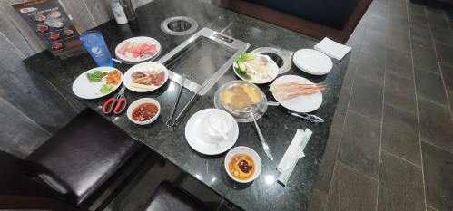 A table set for a hot pot meal, featuring various raw ingredients, sauces, and a cooking pot in the center.