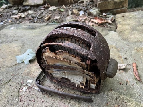 A rusty, disassembled toaster sits on a stone surface, surrounded by leaves and debris.
