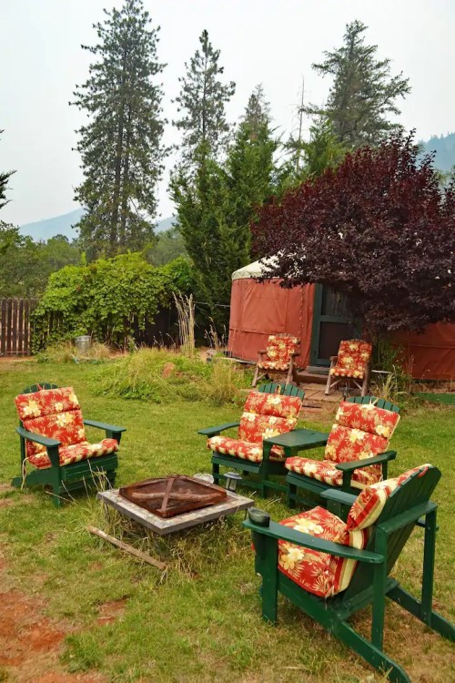 A cozy outdoor seating area with floral chairs around a fire pit, surrounded by trees and greenery.