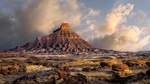 A dramatic landscape featuring a prominent rock formation under a cloudy sky, with textured terrain in the foreground.