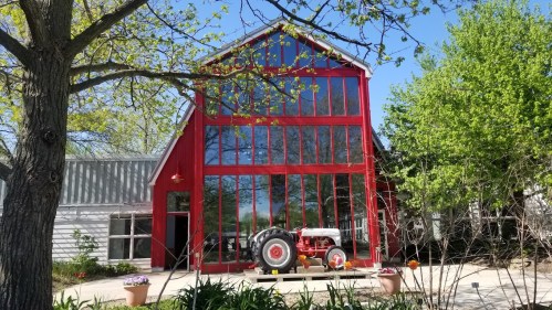 A red barn-style building with large windows, featuring a vintage tractor in front and greenery surrounding it.