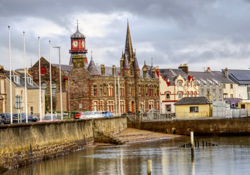 Historic buildings line the waterfront, featuring a clock tower and spires under a cloudy sky.
