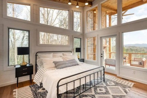 Cozy bedroom with large windows, a metal bed frame, and modern decor, overlooking a scenic outdoor view.