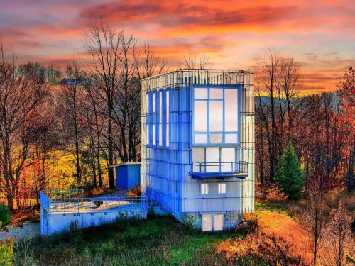 A modern, glass-fronted building surrounded by trees, set against a vibrant sunset sky.