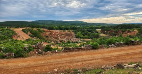 A scenic view of a quarry surrounded by lush greenery and rolling hills under a cloudy sky.