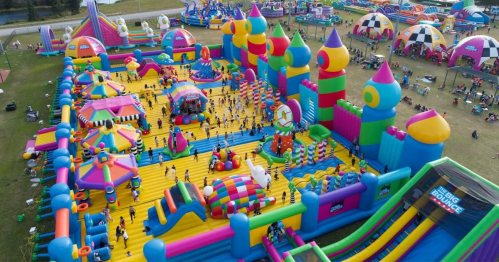 Aerial view of a vibrant inflatable amusement park with colorful bounce houses and slides, filled with people enjoying.