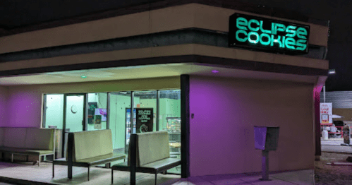 Exterior of Eclipse Cookies shop at night, featuring neon signage and modern seating outside.