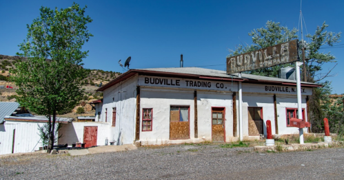 Exterior of Budville Trading Co. building in Budville, NM, featuring a sign and surrounding trees under a clear blue sky.