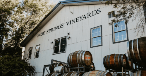 Exterior of Page Springs Vineyards with stacked wine barrels in front of a white building and large windows.