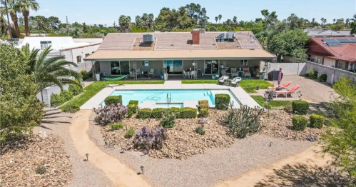 Aerial view of a home with a pool surrounded by landscaped gardens and palm trees in a sunny setting.