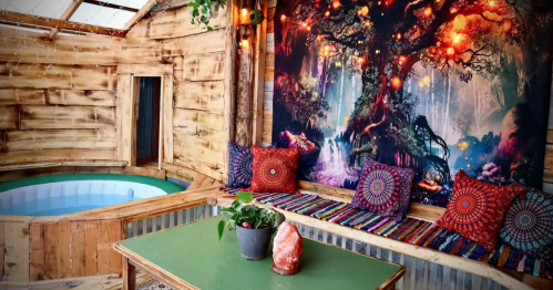 Cozy interior with a hot tub, colorful cushions, a green table, and a vibrant tree mural on the wall.