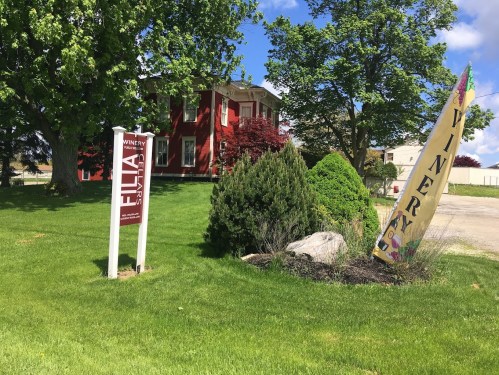A red building with a sign for a winery, surrounded by green grass and trees on a sunny day.