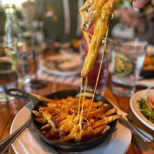 A skillet of cheesy fries with melted cheese stretching as a fork lifts them from the dish.