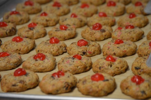 A tray of freshly baked cookies topped with bright red cherries, arranged in neat rows on parchment paper.