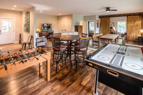 A spacious game room featuring a foosball table, air hockey table, dining area, and comfortable seating.