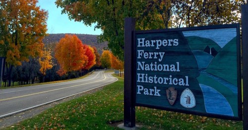 Sign for Harpers Ferry National Historical Park, surrounded by vibrant autumn trees and a winding road.