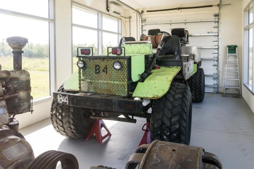 A large, green and black vehicle with oversized tires is parked indoors, surrounded by tools and equipment.