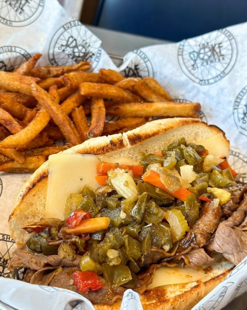 A hearty sandwich filled with beef, cheese, and mixed peppers, served with a side of crispy fries.