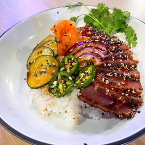 A bowl of rice topped with grilled tuna, sliced vegetables, jalapeños, and garnished with cilantro.