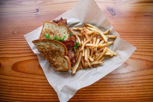 A grilled sandwich with bacon and greens, served with a side of crispy French fries on a wooden table.