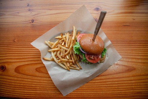 A burger with lettuce, tomato, and onion on a wooden table, accompanied by a side of golden French fries.