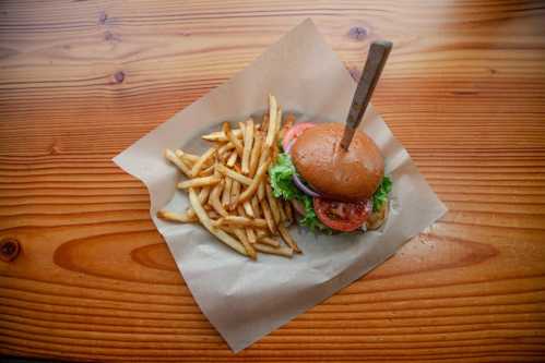 A burger with lettuce, tomato, and onion on a wooden table, accompanied by a side of golden French fries.