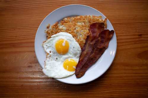 A plate with two sunny-side-up eggs, crispy bacon, and golden hash browns on a wooden table.