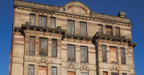 Abandoned building with boarded-up windows and a clear blue sky in the background.