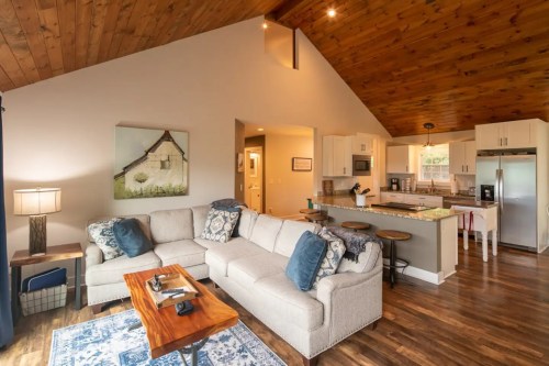 Cozy living room with a sectional sofa, wooden ceiling, and open kitchen featuring modern appliances and a dining area.
