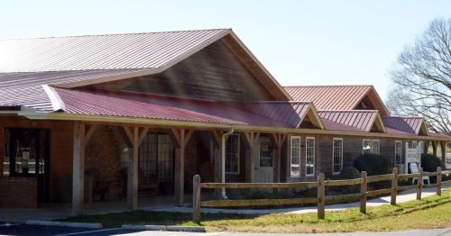 A single-story building with a metal roof, featuring wooden supports and a landscaped entrance.