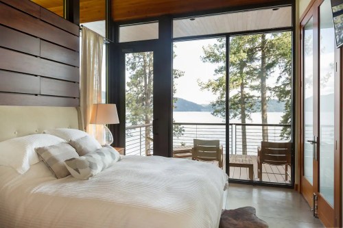 Cozy bedroom with a large window overlooking a lake and trees, featuring a comfortable bed and modern decor.