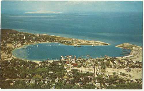 Aerial view of a coastal area with a bay, boats, and scattered houses along the shoreline and lush greenery.