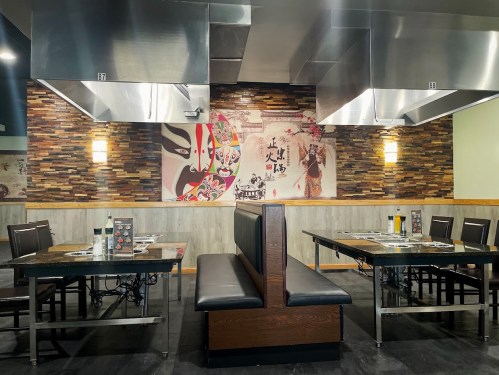 Interior of a restaurant featuring wooden tables, metal exhaust hoods, and a decorative wall mural.