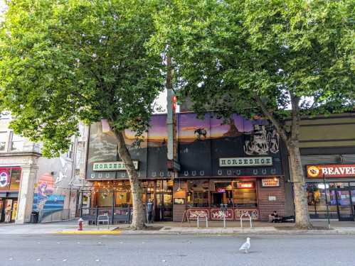 A street view of the Horseshoe bar with large trees in front and a mural on the building, in an urban setting.