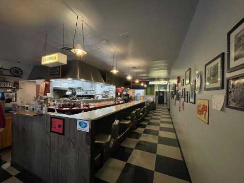 A diner interior featuring a long counter, a cashier area, and black-and-white checkered flooring.