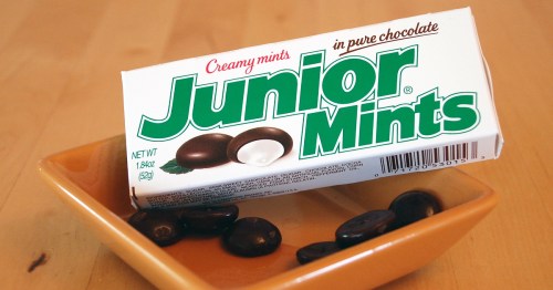 A box of Junior Mints with creamy mints in pure chocolate, placed next to a small dish of mints.