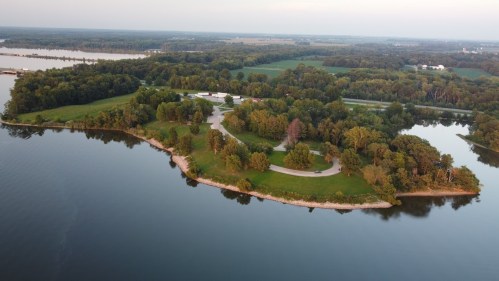 Aerial view of a lush green island surrounded by calm water, with trees and a winding path visible.