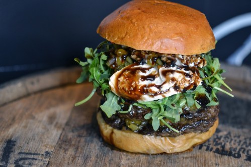 A gourmet burger with a juicy patty, melted cheese, arugula, and a drizzle of sauce, served on a toasted bun.