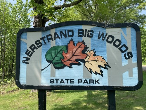 Sign for Nerstrand Big Woods State Park featuring colorful leaves and surrounded by greenery.