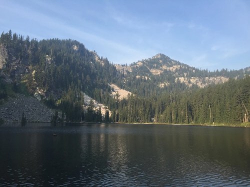 A serene lake surrounded by lush green forests and mountains under a clear blue sky.